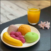 Load image into Gallery viewer, Colorful chocolate shaped like fruits and a glass of orange juice on a dark surface.