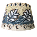 A conical lampshade featuring a hand-painted foliage design with whimsical patterns in beige, black, and blue colors.