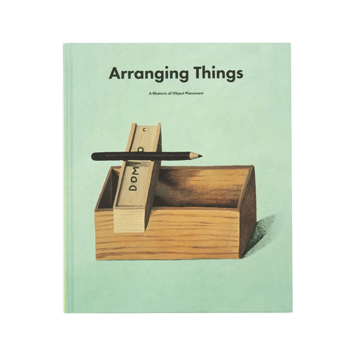 Mint green book titled ‘Arranging Things’ with a minimalist cover design featuring a wooden box, stacked blocks, and a pencil balanced across the top.