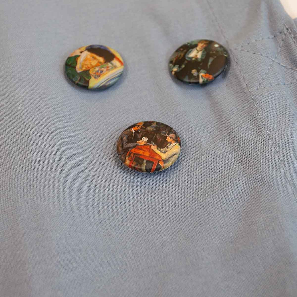 Three round buttons with artistic designs on a light gray fabric background