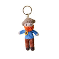 Crocheted keychain with a character wearing a blue shirt, orange scarf, and brown pants on a white background.