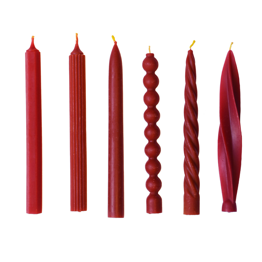 A collection of red beeswax dinner candles in assorted shapes, displayed side by side.